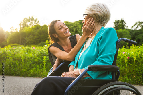 Granddaughter smiling while looking at grandmother sitting in wheelchair photo