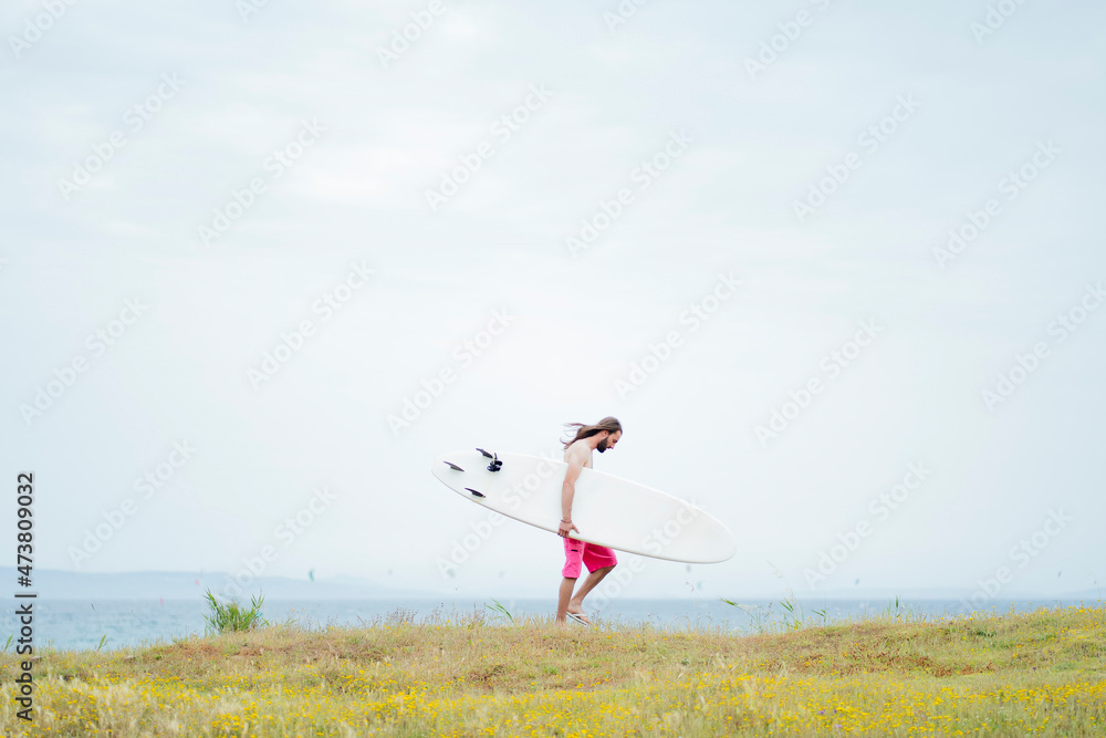 Man carrying surfboard while walking on meadow Man carrying surfboard while walking on meadow