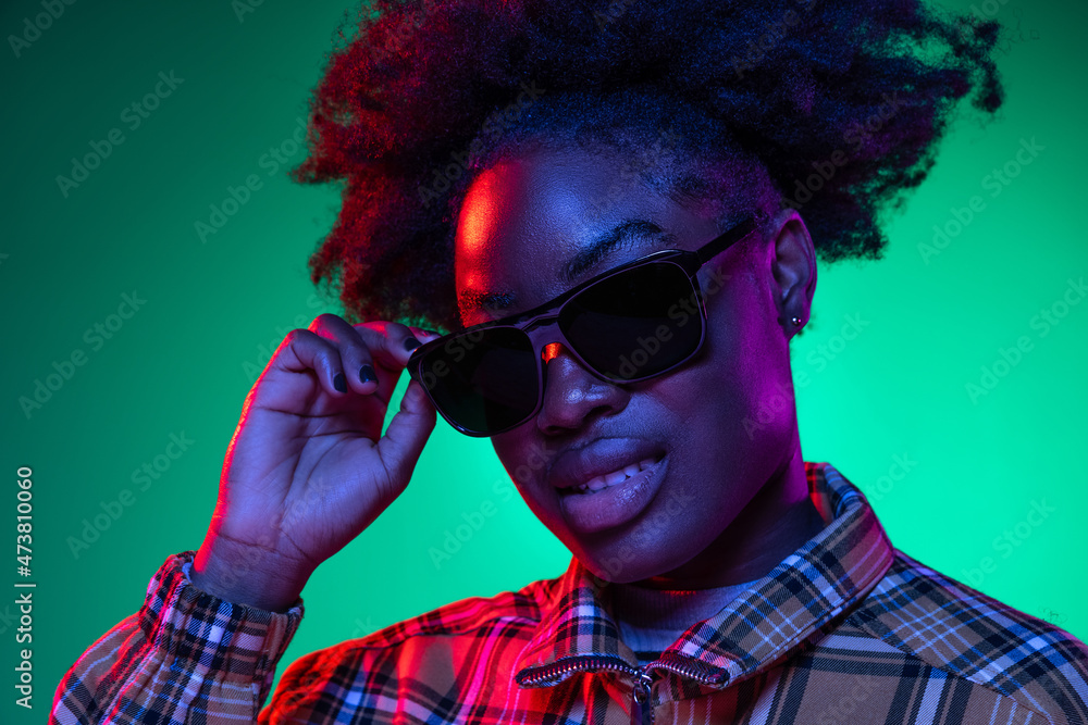 Close-up young beautiful girl in eyeglasses on dark green studio background in purple neon light. Concept of human emotions