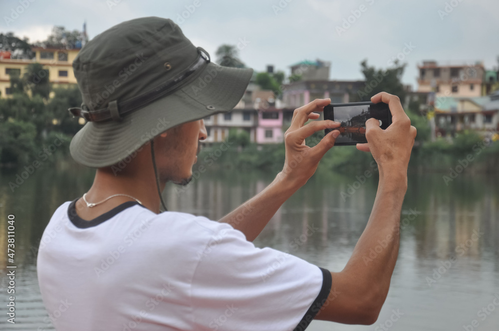 Obraz premium Back view of a male tourist taking photo of landscape with smartphone during cloudy weather
