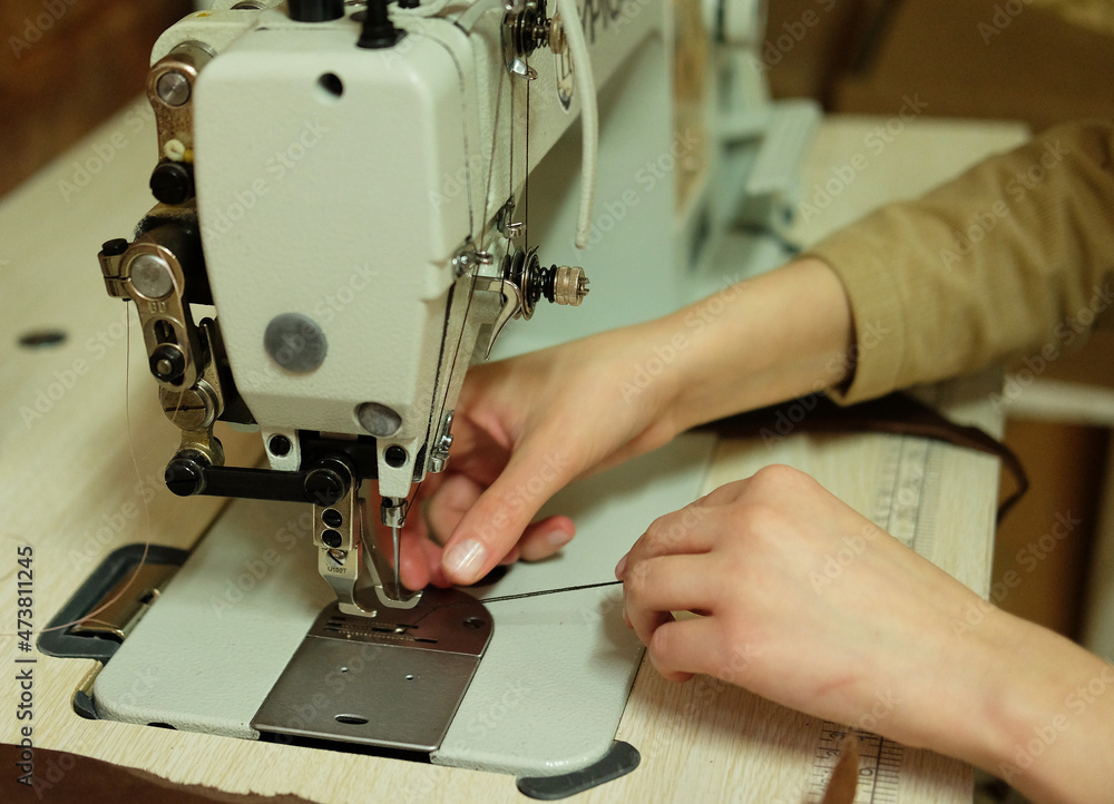 Young woman sews the details of a bag on a sewing machine