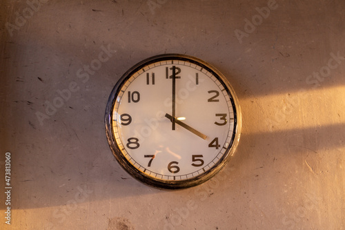 wall clock on the concrete wall at 4pm with sunlight on the right hand side