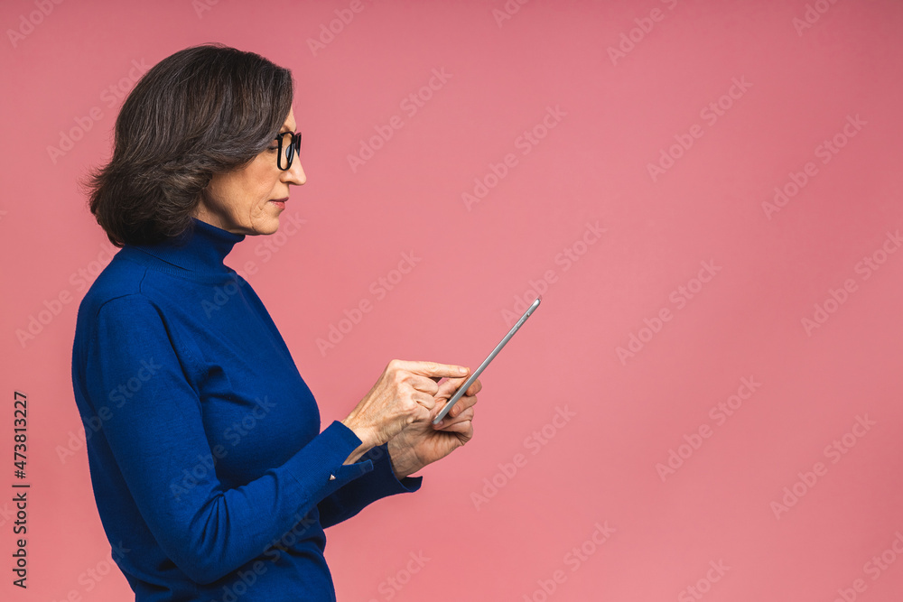 Portrait of smiling beautiful senior aged mature woman using tablet computer, isolated over pink background. Copy space for text. Portrait of smiling beautiful senior aged mature woman using tablet computer, isolated over pink background. Copy space for text.