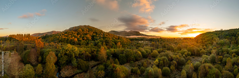 Aerial view looking across a large pine forest with mountains at sunrise with early morning mist, Scotland panoramic