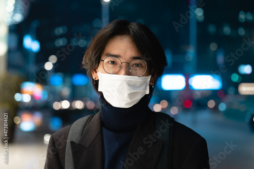 Portrait of an Asian businessman wearing a mask, in the street at night