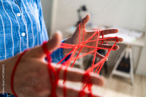 Female entrepreneur making cats cradle with woolen string in office photo