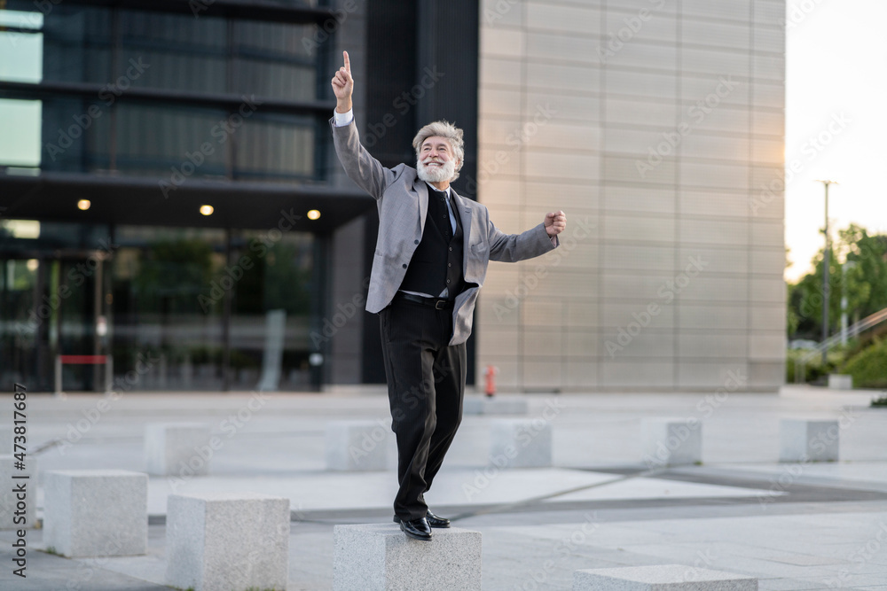 Cheerful businessman dancing on concrete block by office building Cheerful businessman dancing on concrete block by office building