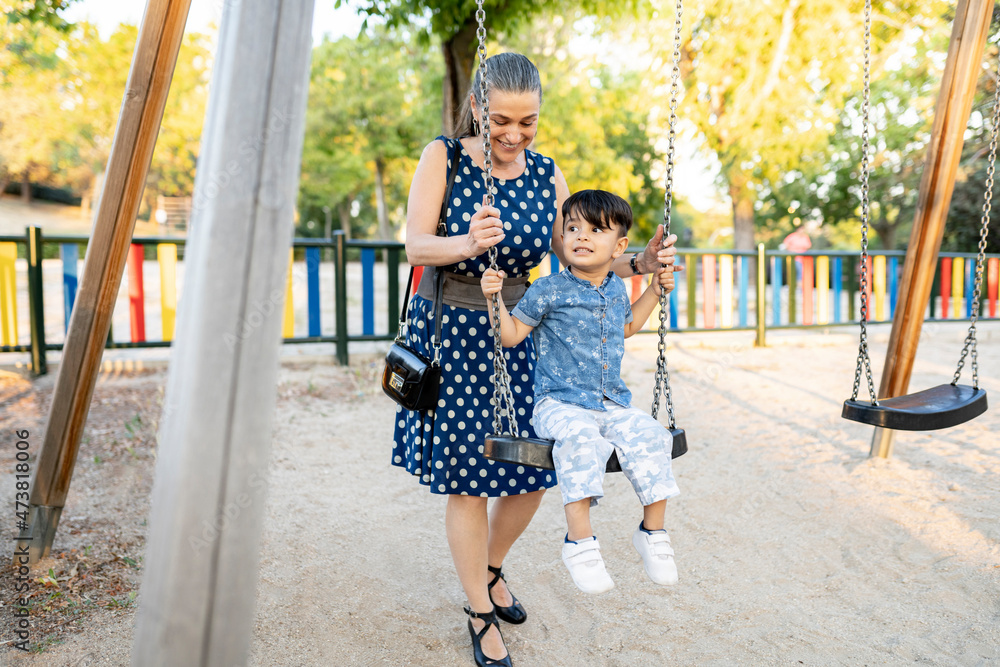 Boy looking away while grandmother pushing swing at playground during sunset Boy looking away while grandmother pushing swing at playground during sunset
