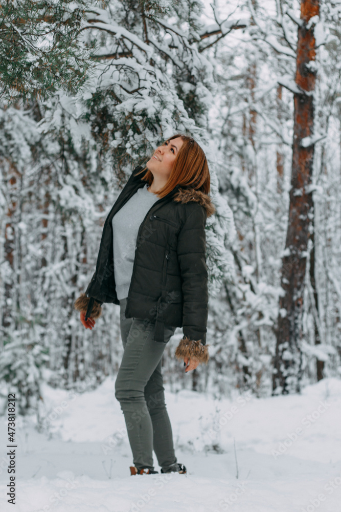 A happy girl with a short haircut walks in the forest after a snowfall and admires the incredible nature. Winter fairy tale in the forest. Christmas holidays, outdoor activities