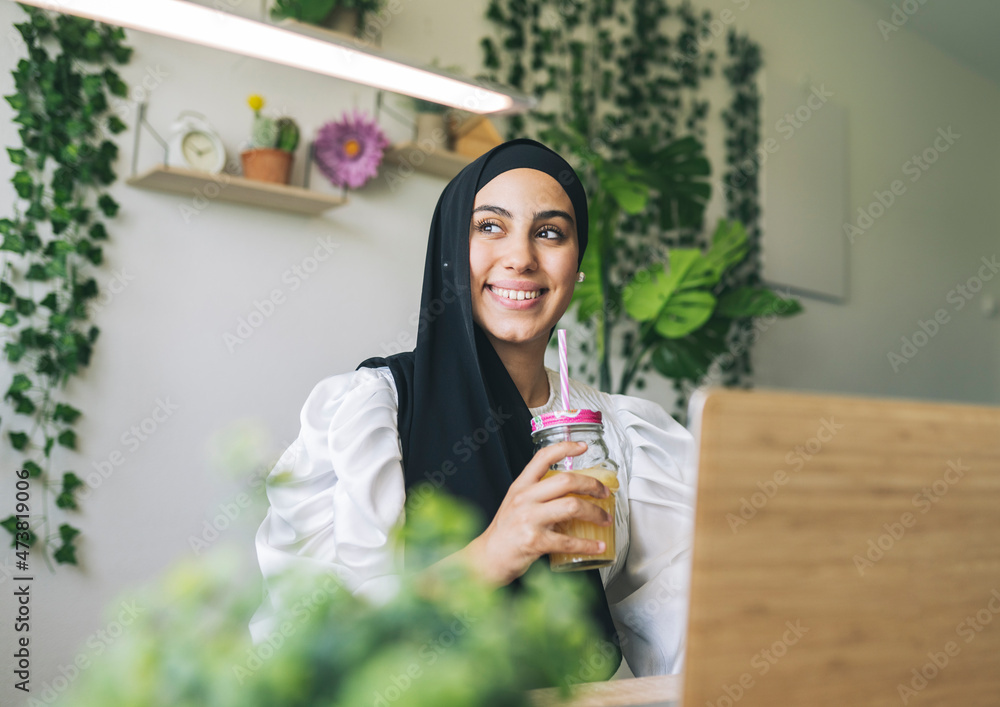 Smiling female freelancer looking away while having juice at home Smiling female freelancer looking away while having juice at home