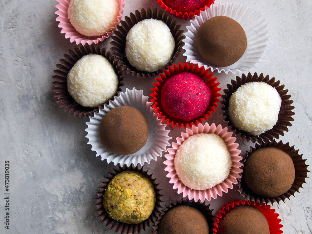Top view on truffle sweets in wrappers. Different types of candy: dark chocolate truffle in cocoa, white coconut truffle, red candy covered with sublimated raspberries, candy covered in nut crumbs. Top view on truffle sweets in wrappers. Different types of candy: dark chocolate truffle in cocoa, white coconut truffle, red candy covered with sublimated raspberries, candy covered in nut crumbs.
