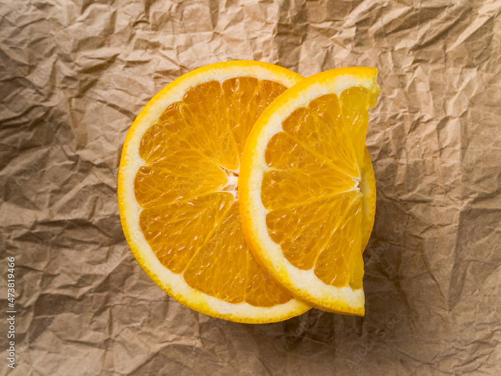 Top view of half an orange on which lies a slice of fruit. Natural sweet dessert lies on dark brown crumpled kraft paper. Top view of half an orange on which lies a slice of fruit. Natural sweet dessert lies on dark brown crumpled kraft paper.