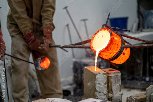 Manual workers pouring molten bronze in container at foundry photo