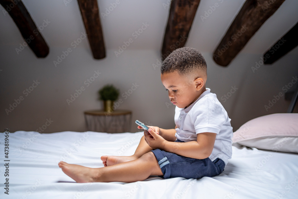 Boy using smart phone while sitting on bed at home