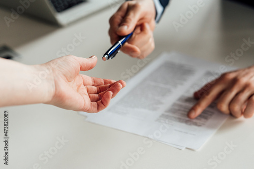 Businessman giving pen to woman with contract in background at office
