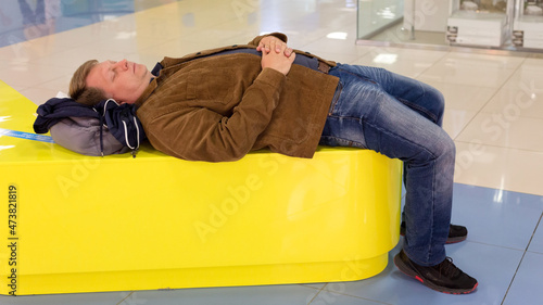A tired man in a corduroy jacket lay down exhausted on a soft leather sofa in a shopping center after shopping.