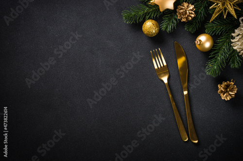 Christmas table with golden cutlery and christmas decorations at black background. CHristmas food concept. Top view with copy space.