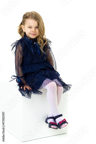 Charming little girl sitting on white cube studio