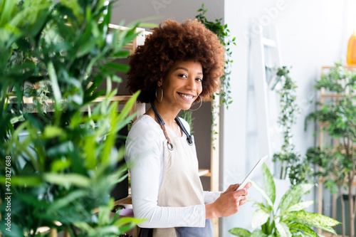 Female shop owner holding digital tablet while standing at plant store