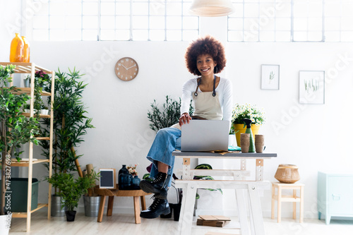 Smiling female shop owner sitting with laptop in plant store