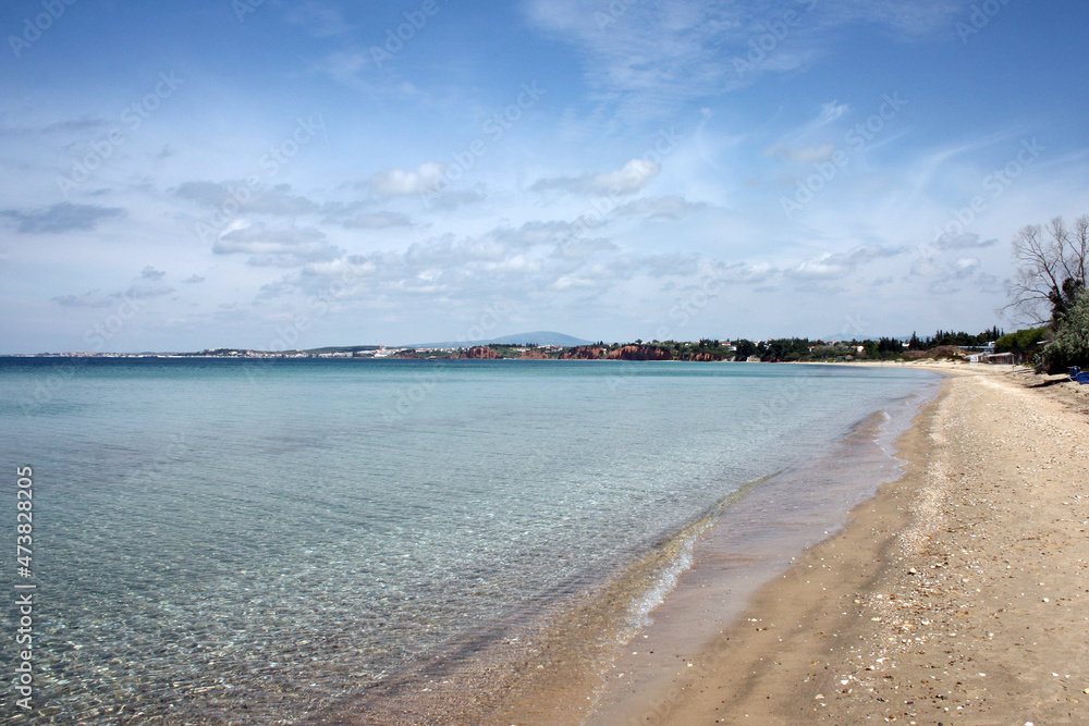 Sandy seashore. Calm, not deep, azure sea. In the distance are the mountains and the city. Picturesque water landscape.