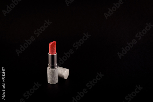 Red lipstick with glitter in a silver bottle cap next to the bottle on a black background side view