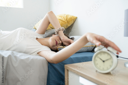 Woman snoozing alarm while sleeping on bed at home