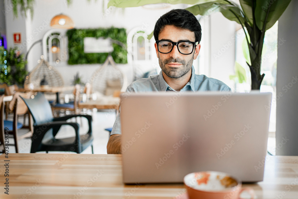 Young male freelancer using laptop at table in cafe Young male freelancer using laptop at table in cafe