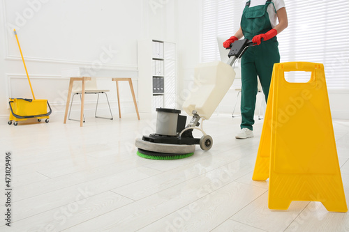 Professional janitor cleaning parquet floor with polishing machine in office, closeup photo
