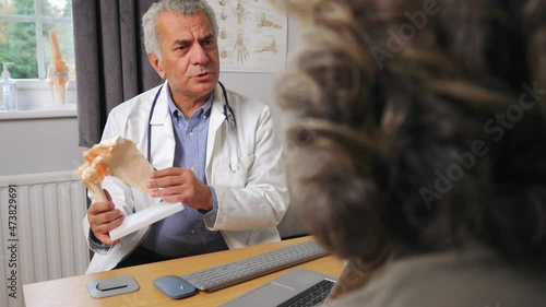 Mature Male Doctor Meeting With Female Patient Discussing Joint Pain In Hip Using Anatomical Model photo