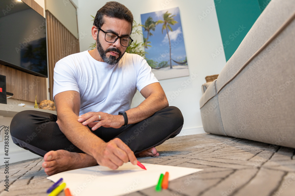 man practicing art therapy, sitting in the living room of his house, with green crayons in his hands, the plant in the background. man practicing art therapy, sitting in the living room of his house, with green crayons in his hands, the plant in the background.