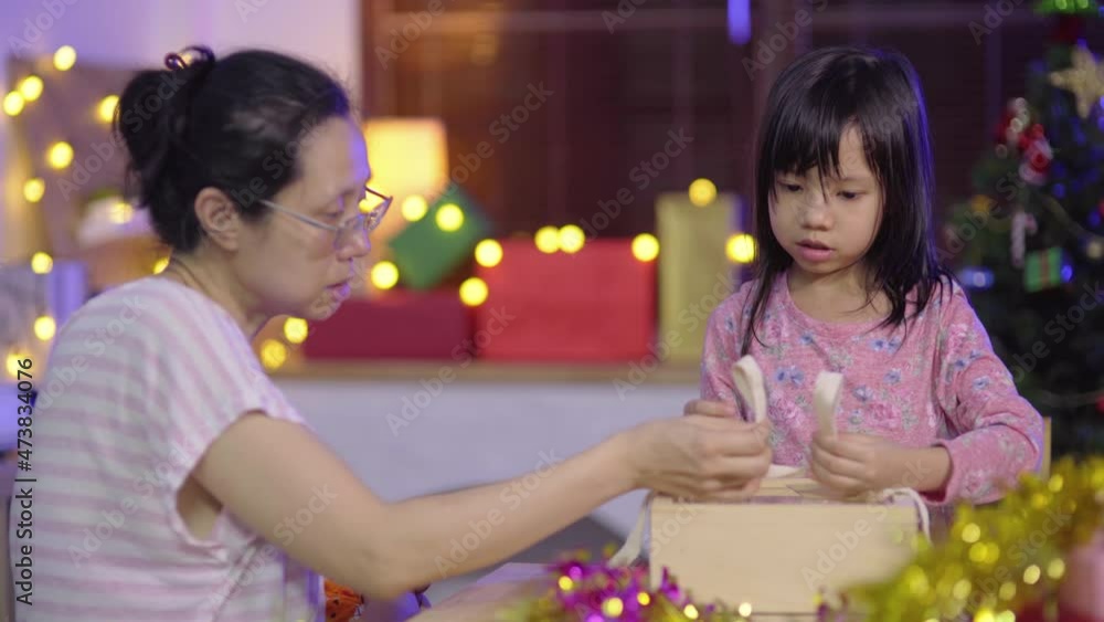 Asian family with woman as mother teach her child to wrapping a present gift box for surprise and celebrate Christmas holidays and New year party together at home Asian family with woman as mother teach her child to wrapping a present gift box for surprise and celebrate Christmas holidays and New year party together at home