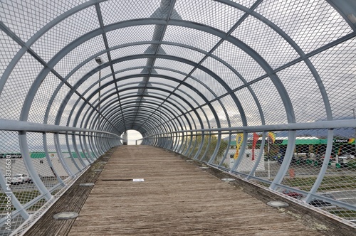 Metal tunnel bridge with wooden walkway.Strong metal bars bridge in shape of tunnel with wooden walkway and round floor lights on both sides.circular arch tunnel of metal construction.