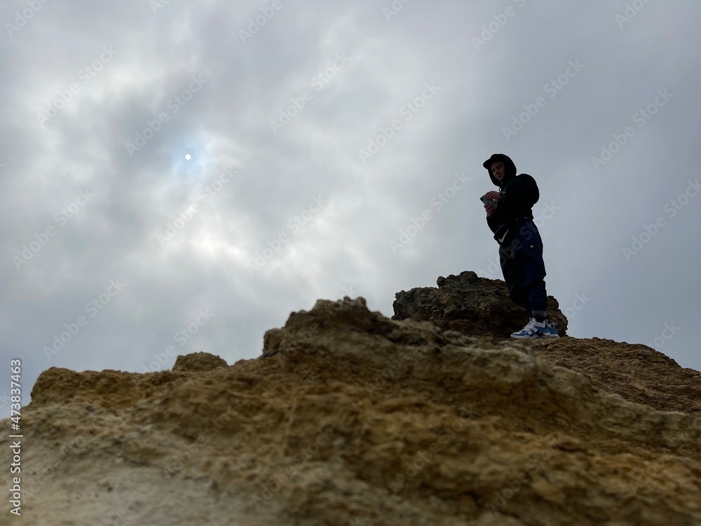 Low angle shot of a climber on top of a yellow rock under cloudy grey sky