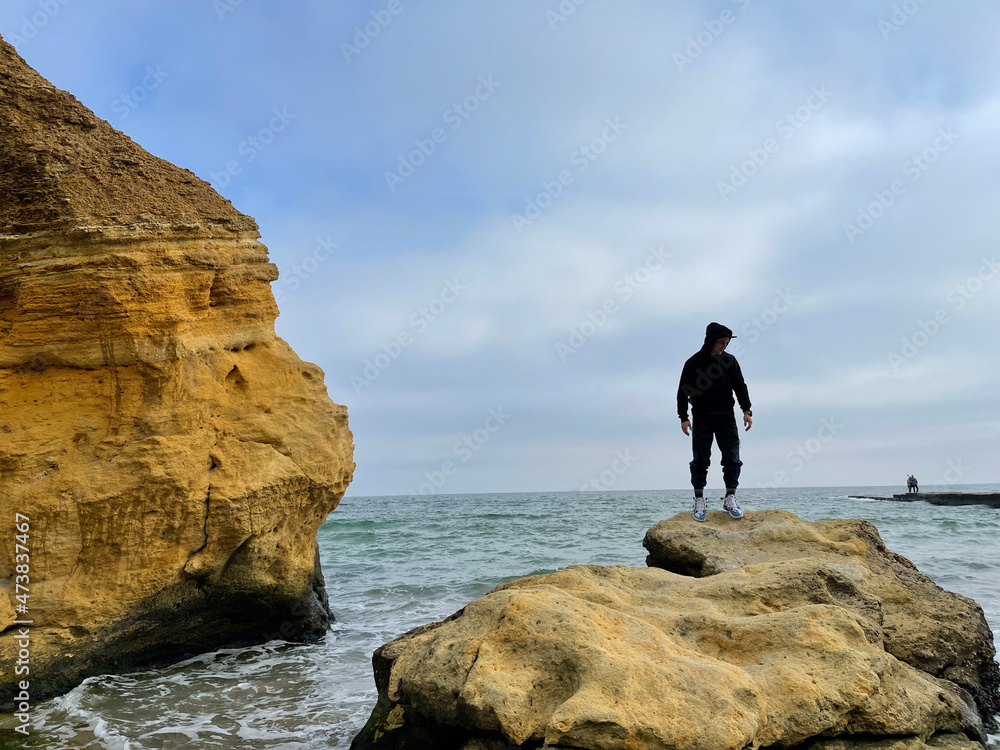 Man in black clothing standing on top of a rock on the seashore