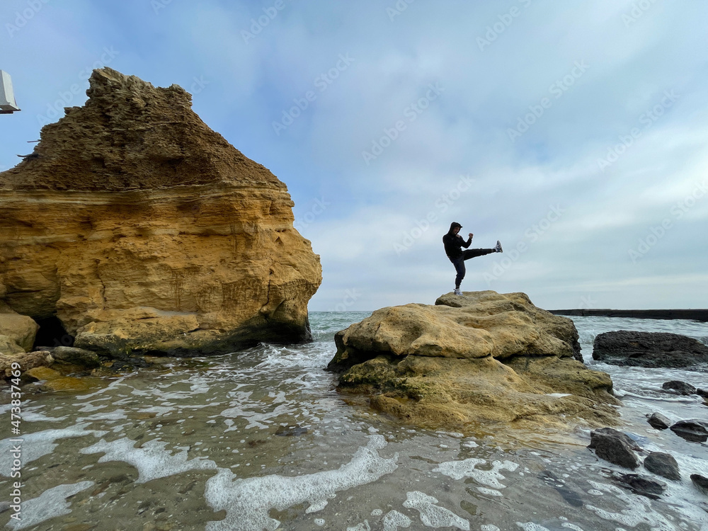 Obraz premium Man standing in karate or kungfu stance on top of a rock in the sea