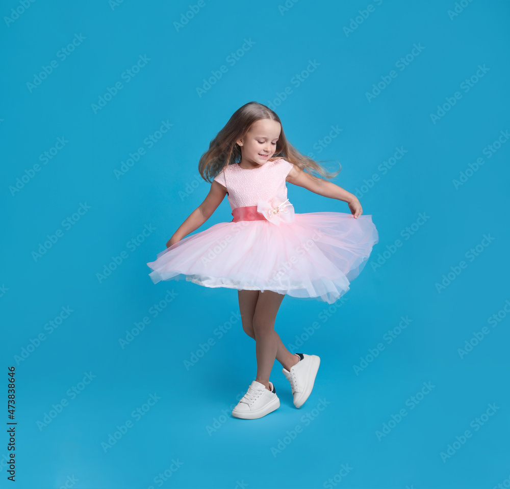 Cute little girl in beautiful dress dancing on light blue background Cute little girl in beautiful dress dancing on light blue background