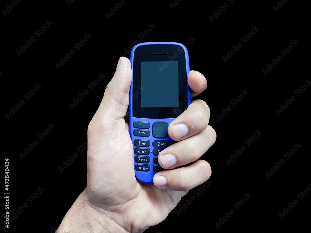 A person holding old feature phone in hand with isolated black background. A person holding old feature phone in hand with isolated black background.