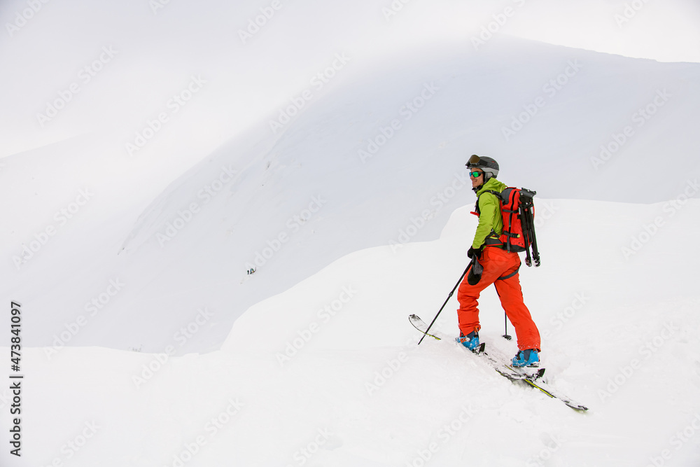 view of man skier with trekking poles walking along snowy mountain slope