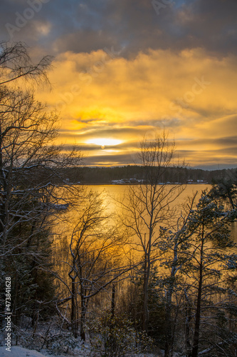 Color full winter sun in solstice reflex in the calm lake Mälaren and trees in silhouette a winter day with snow in Stockholm