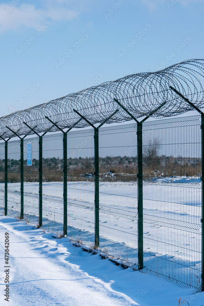 Iron fence with barbed wire in a snow-covered winter field against a blue sky. Fenced guarded territory, no access. Area protection and counteraction to illegal entry concept Iron fence with barbed wire in a snow-covered winter field against a blue sky. Fenced guarded territory, no access. Area protection and counteraction to illegal entry concept
