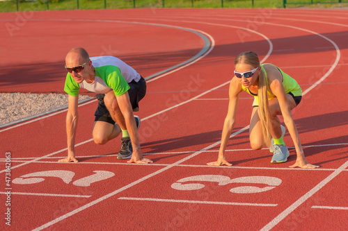 Konstfotografi Athletic woman and man on the track of the stadium preparing for the start, starting to run