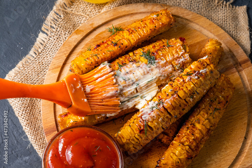 Grilled corn with spices is smeared with a brush with butter, close-up.