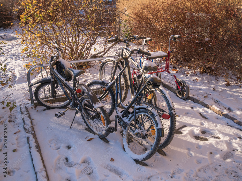 Snowy bikes and a walker at a park lot a cold and sunny pale winter day in Stockholm