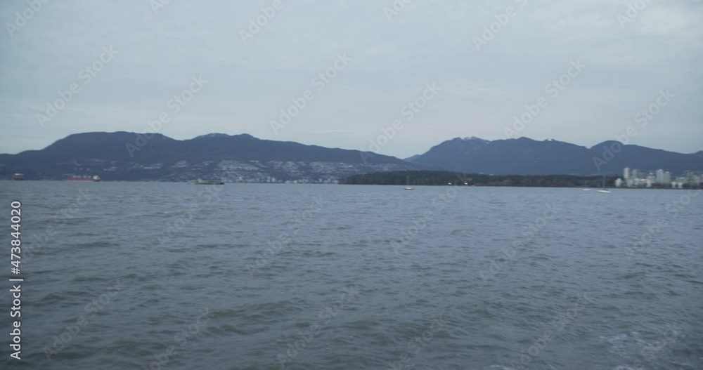 A landscape shot of the sea waves washing on the sand at Vancouver's coast with the cargo ferries and mountain range on the background A landscape shot of the sea waves washing on the sand at Vancouver's coast with the cargo ferries and mountain range on the background