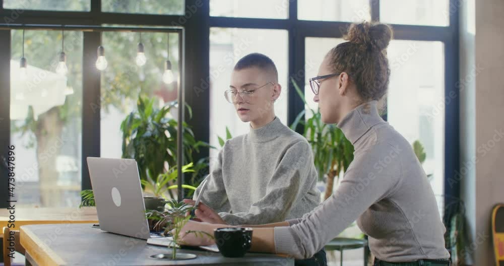 Two young female students study online while sitting in a modern coffee shop Two young female students study online while sitting in a modern coffee shop