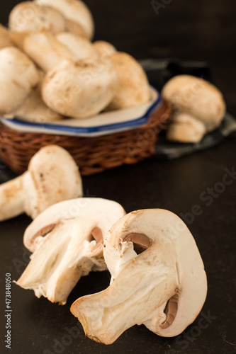 Cut champignon and some mushrooms in a basket on a black wooden table 