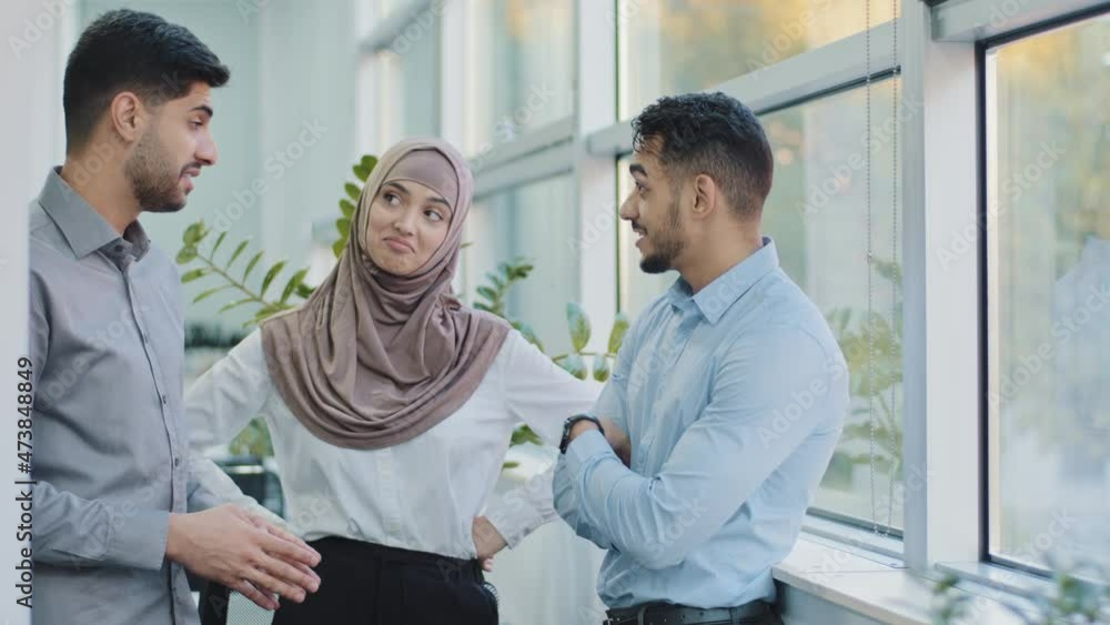 Three diverse professional colleagues talking in modern office, happy friendly arab muslim woman in hijab and two Indian men coworkers having conversation discuss business project at work space Three diverse professional colleagues talking in modern office, happy friendly arab muslim woman in hijab and two Indian men coworkers having conversation discuss business project at work space