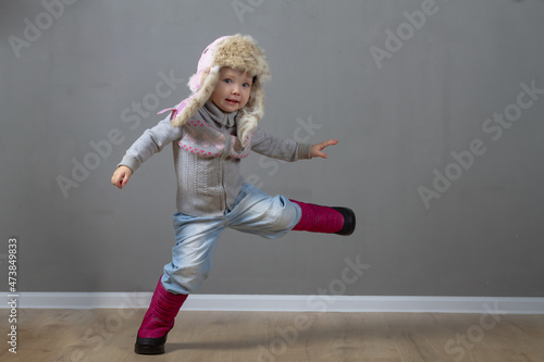 Cute baby girl 2 years old caucasian in warm winter clothes and a hat with earflaps with fur on a gray background