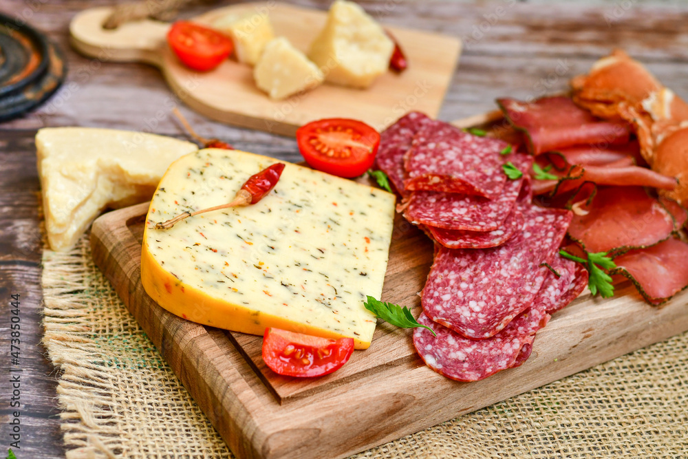 Italian dried thinly sliced artisan pork salami Milano , parmesan cheese, tomatoes and fresh basil on wooden background .Rustic home made italian snack. Italian dried thinly sliced artisan pork salami Milano , parmesan cheese, tomatoes and fresh basil on wooden background .Rustic home made italian snack.
